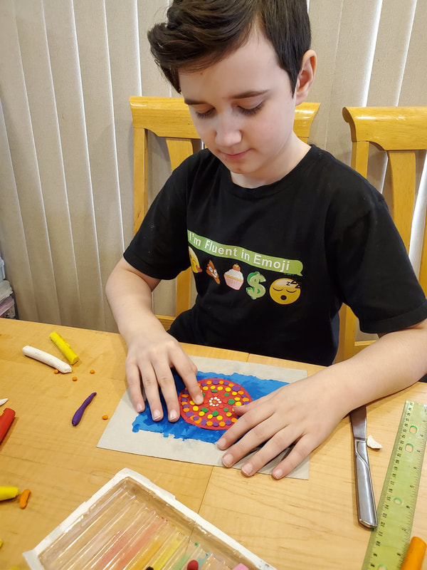 Boy sitting at a table creating art with plasticine.
