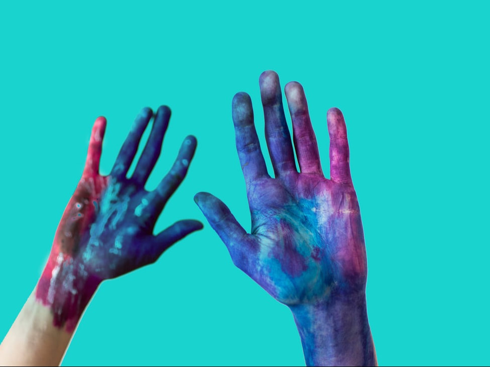 Artist's hands are raised up, covered in colourful paint.